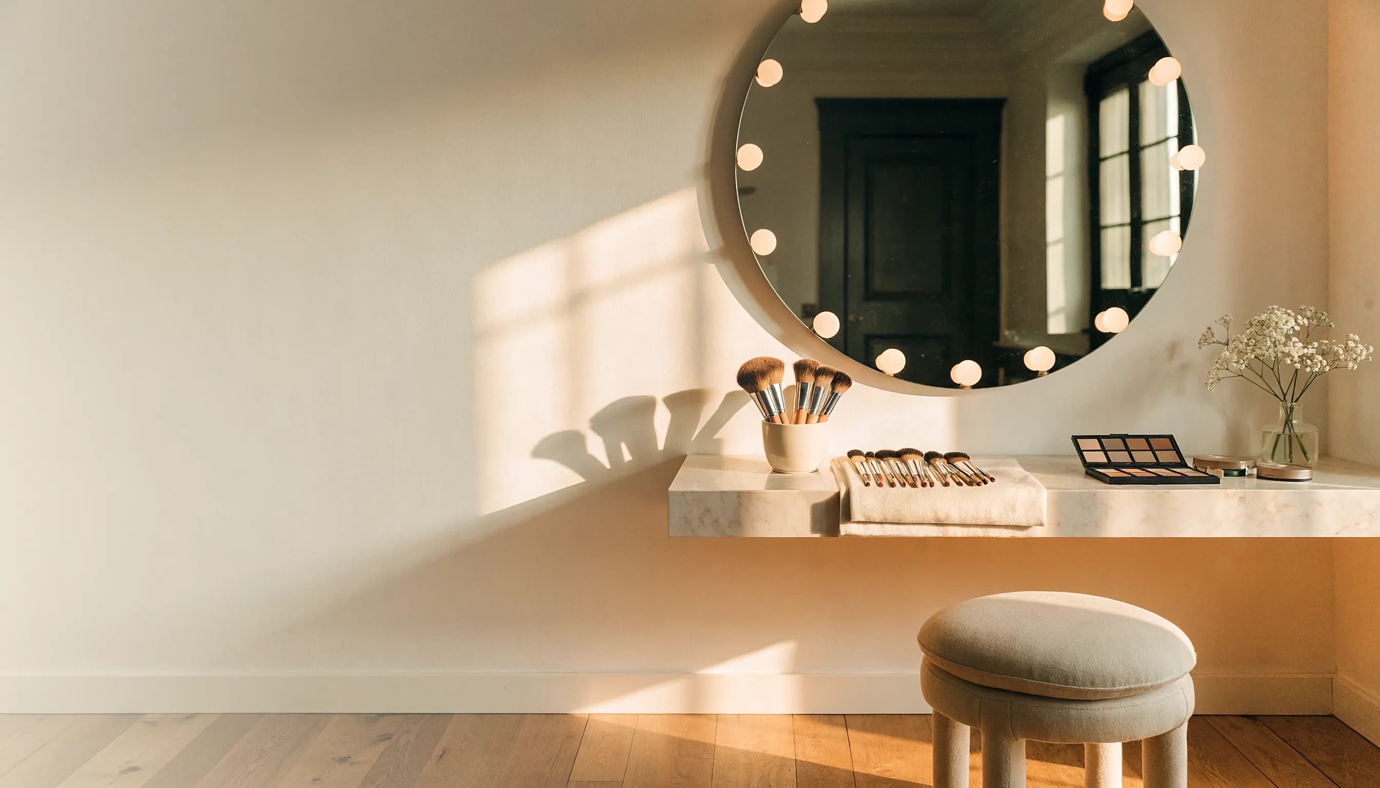 A makeup station at golden hour, brushes laid out beneath a bulb-ringed mirror