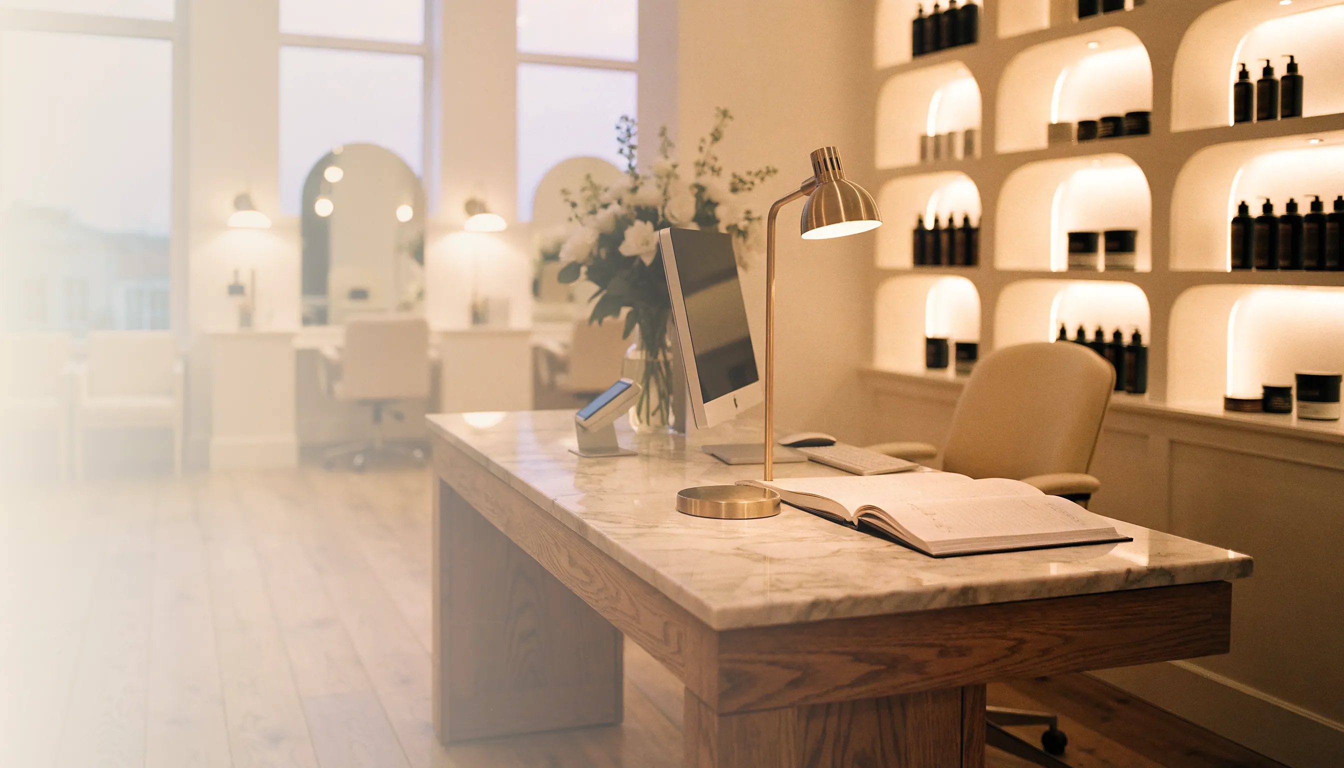 A salon reception desk at dusk with the lamps on and a phone lit on the counter